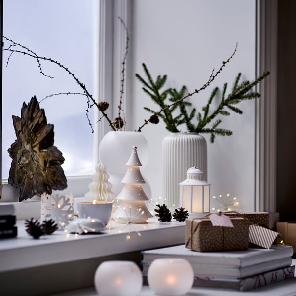 A windowsill is decorated with white-themed VINTERFINT ornaments and a STRÅLA lighting chain.