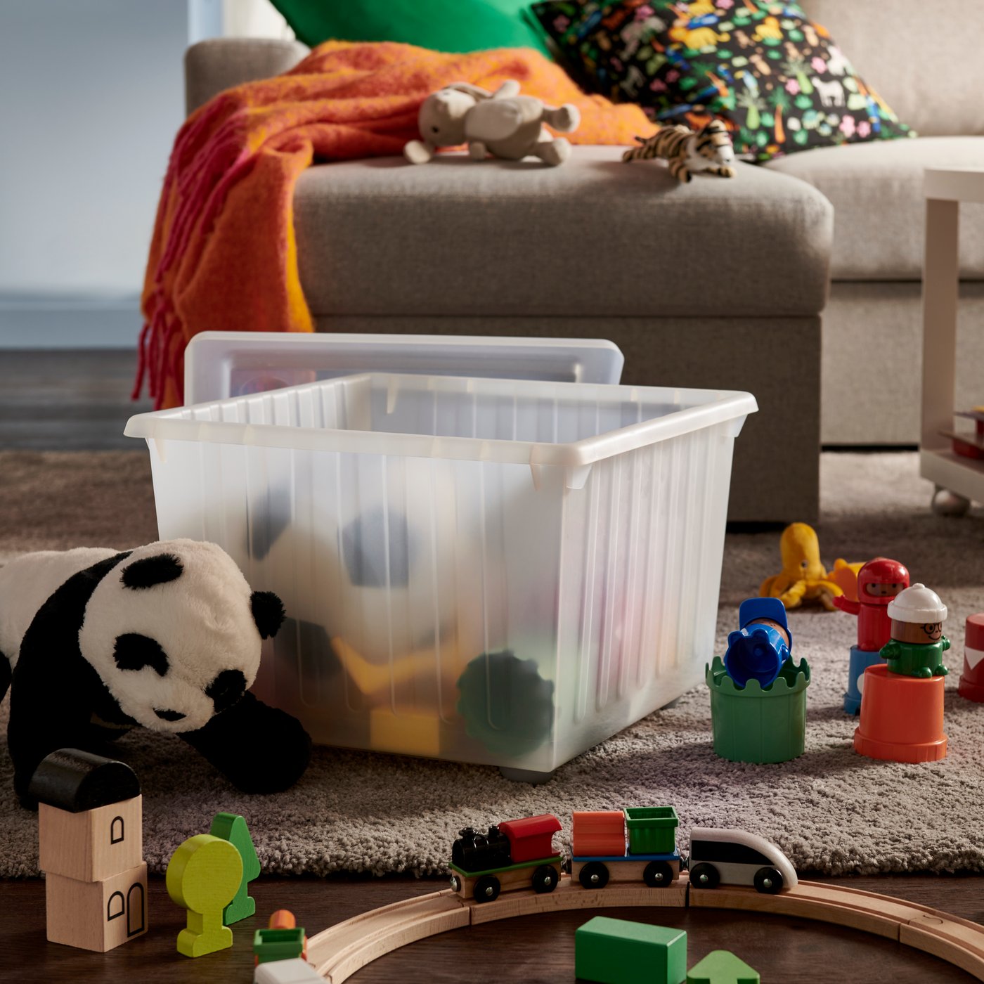 A softly sunlit living room featuring a white VESSLA storage crate with castors, surrounded by a sofa and toys.