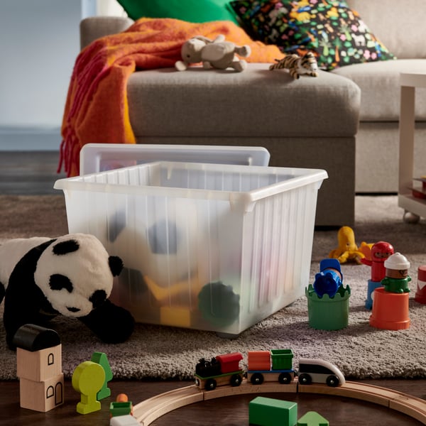 Es ist ein tageshelles Wohnzimmer mit einem weißen VESSLA Kasten auf Rollen mit Abdeckung umgeben von einem Sofa und Spielzeug zu sehen.