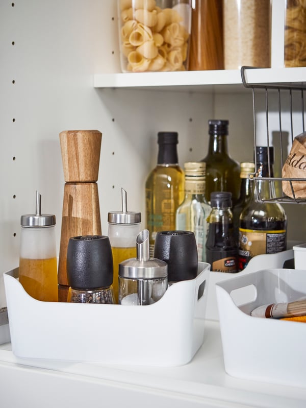 Gambar dekat kotak plastik VARIERA berwarna putih yang menyimpan perasa seperti botol minyak dan sos di dalam kabinet dapur.