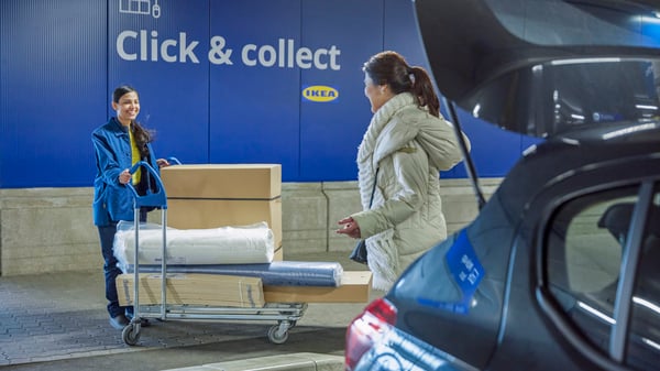 En kvinde står ved sin bil, mens en IKEA-medarbejder bringer hendes bestillinger på en indkøbsvogn i et 