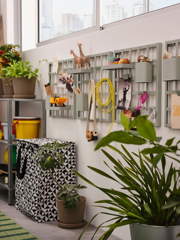 A row of grey-green SNICKRA storage boards on an enclosed balcony wall, holding various items, plus a black/white bag and plants.