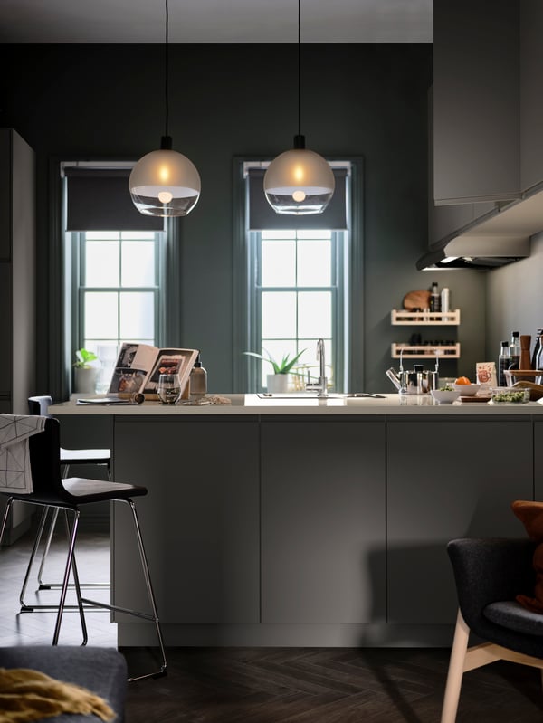 Una cocina en la que una barra de cocina sobresale para formar una península revestida con taburetes de bar BERNHARD e iluminada con lámparas JAKOBSBYN de techo.