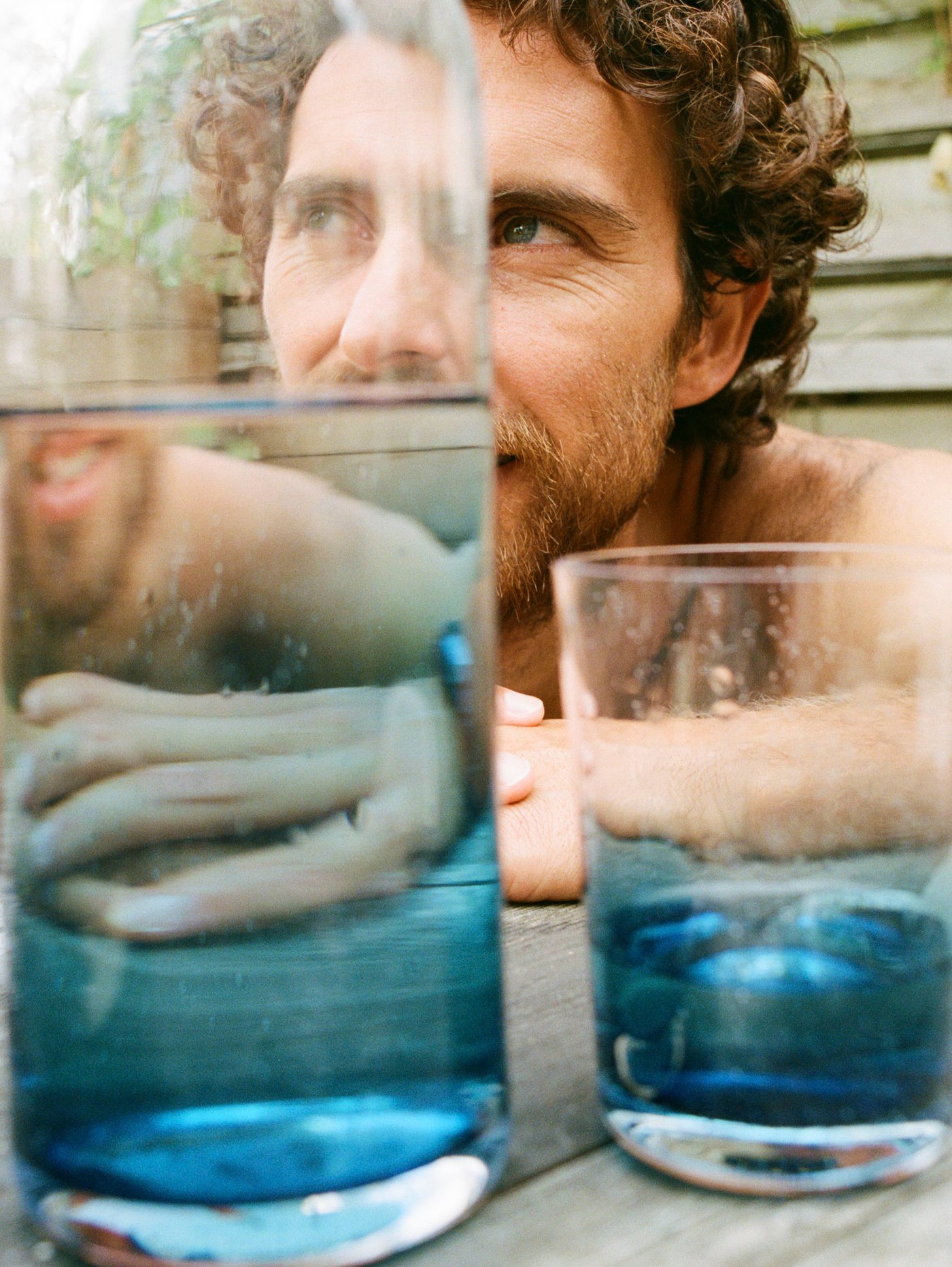KÅSEBERGA glass and carafe made with a gradient of blue and clear glass placed in front of a man leaning on the table behind.