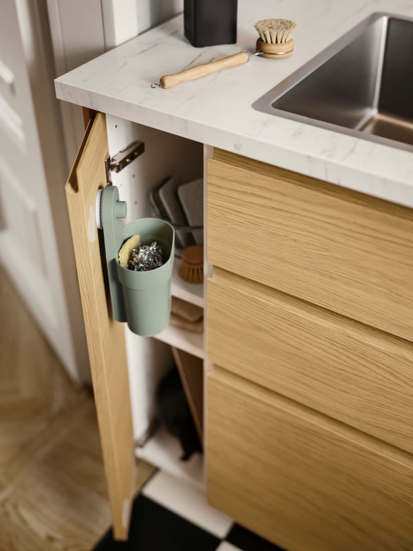 A grey-green ÖBONÄS container with suction cup is mounted on the inside of an opened VOXTORP cabinet door with oak effect.
