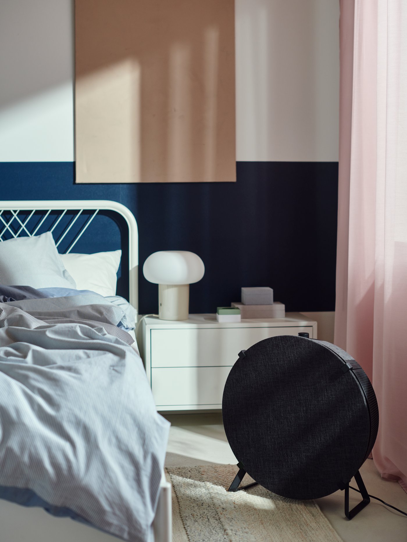 Black air purifier placed beside a bed in a modern bedroom setting.