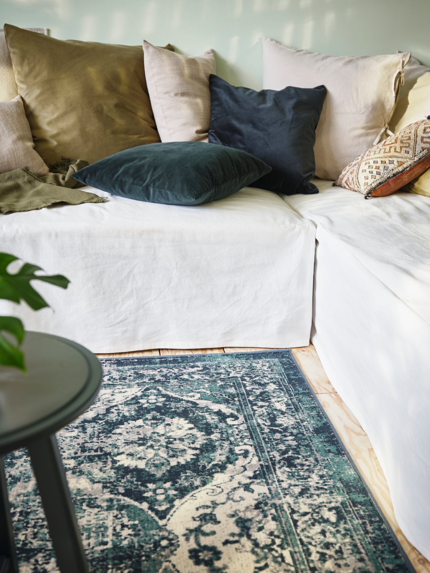 Seating in an L-shape, beside a VONSBÄK rug, with covers that reach to the floor and lots of cushions on top of the seating.