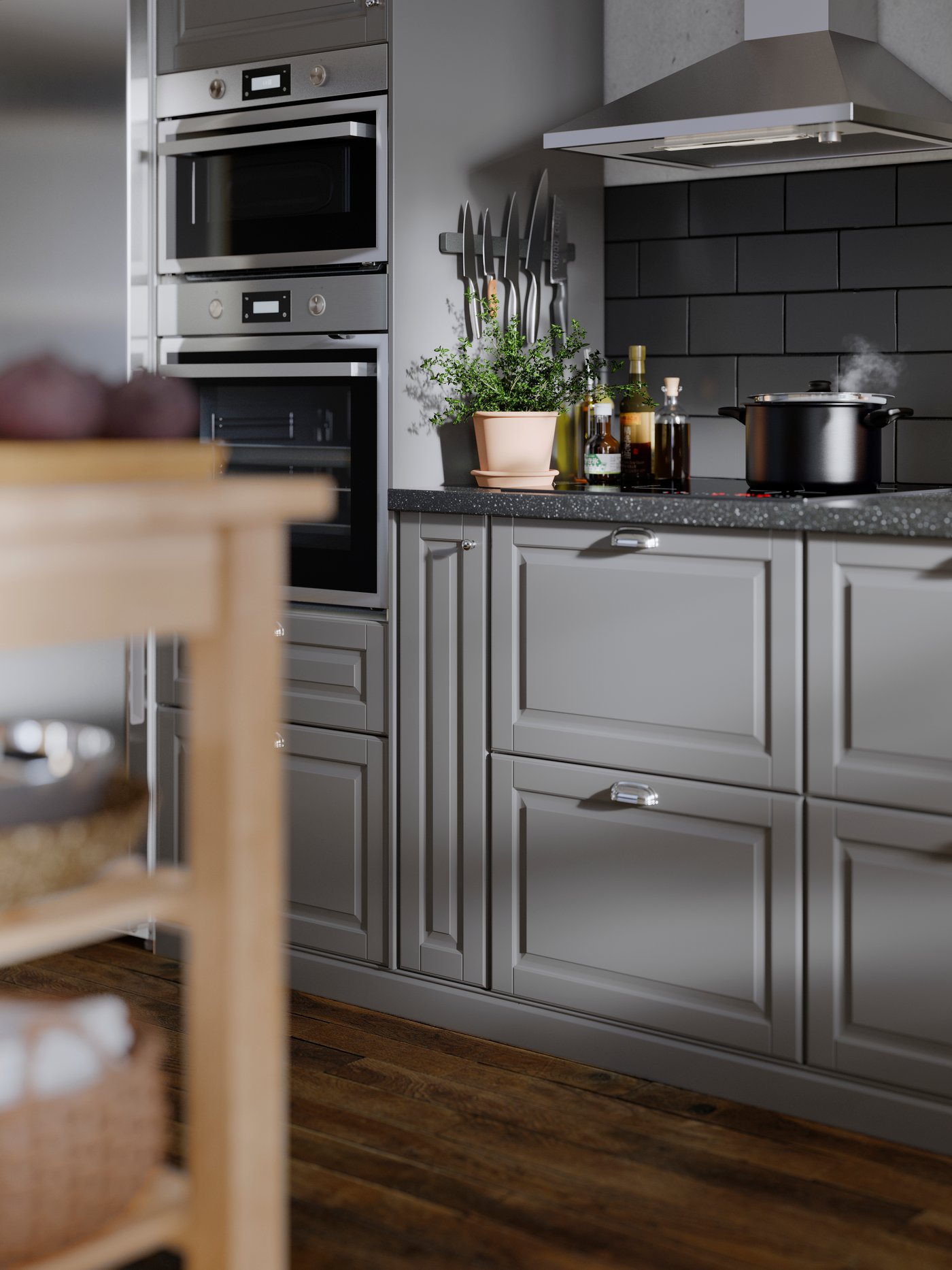 A kitchen with grey tiles and a brown floor has grey BODBYN fronts with bevelled panels and appliances in stainless steel.