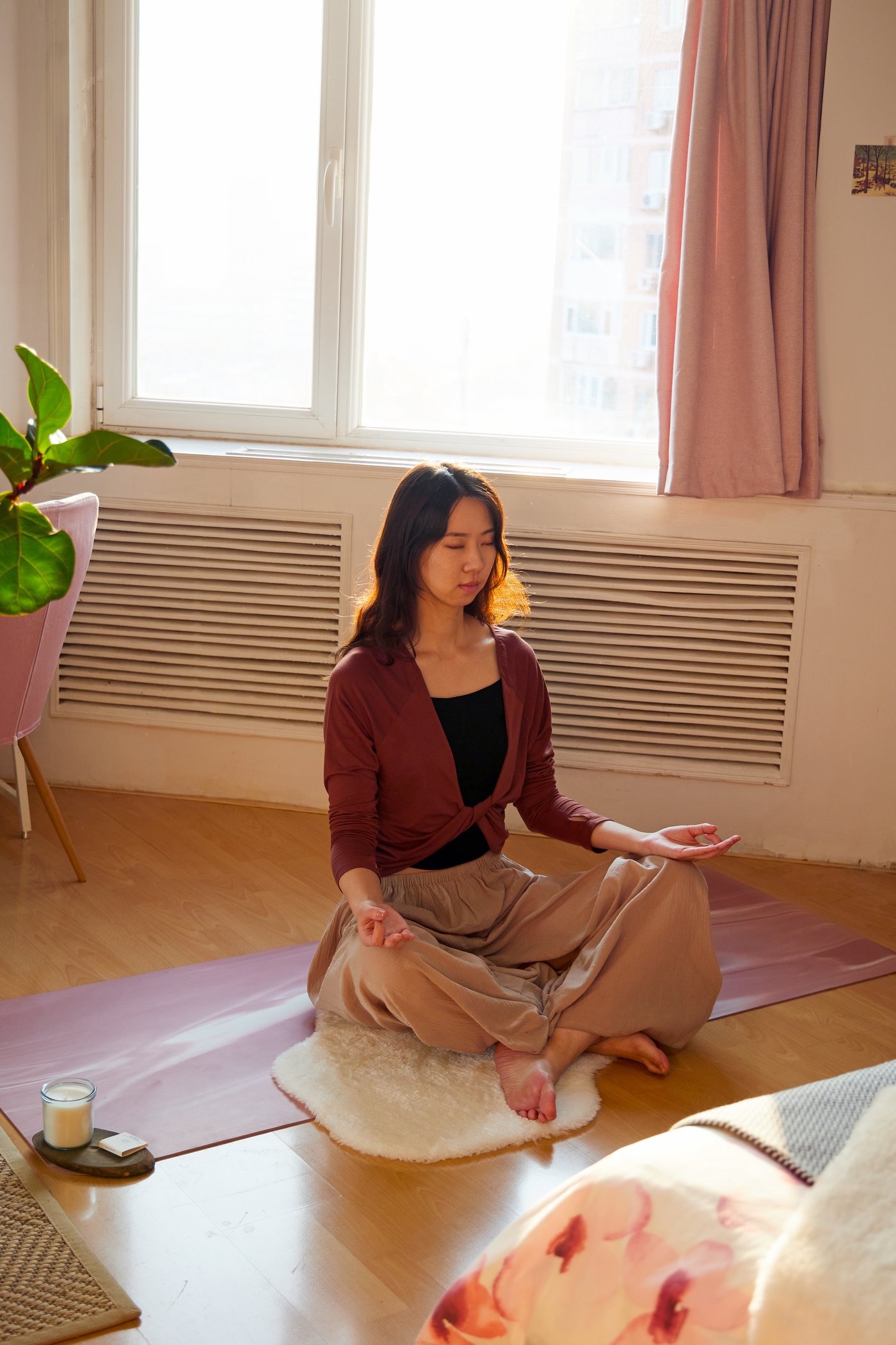 Žena meditira na podu u svojoj sobi pored prozora, a kao oslonac koristi mekani beli TOFTLUND tepih.