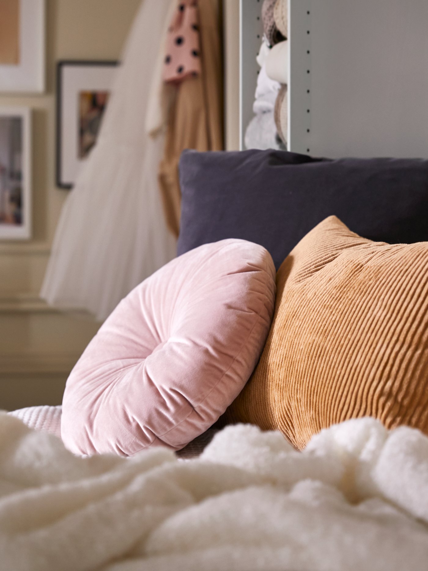 Un coussin KRANSBORRE rose clair et un autre coussin dans une housse ÅSVEIG beige foncé posés contre un coussin gris foncé.