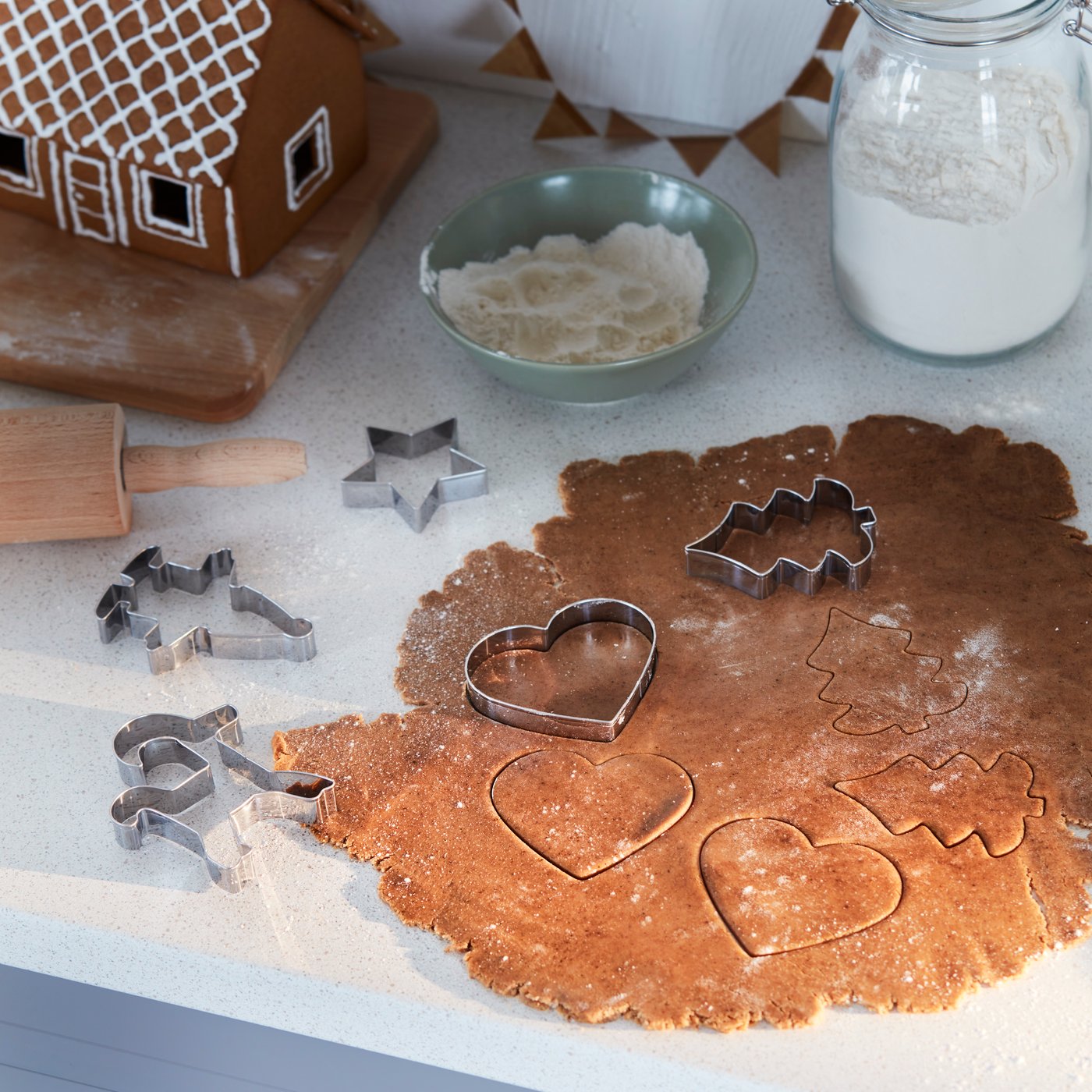 Una masa extendida sobre una cubierta blanca, con moldes en forma de corazón y árbol de navidad para cortar galletas. 