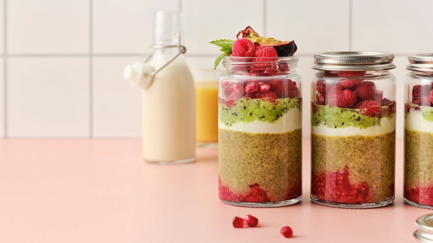 Chiabudding, røde bær, yoghurt og kiwi ligger i lag i et glas med en skive passionsfrugt og mynteblade på toppen.