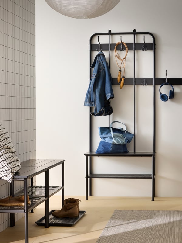 Traditional style black coat rack and bench with shoe storage in hallway with white walls.