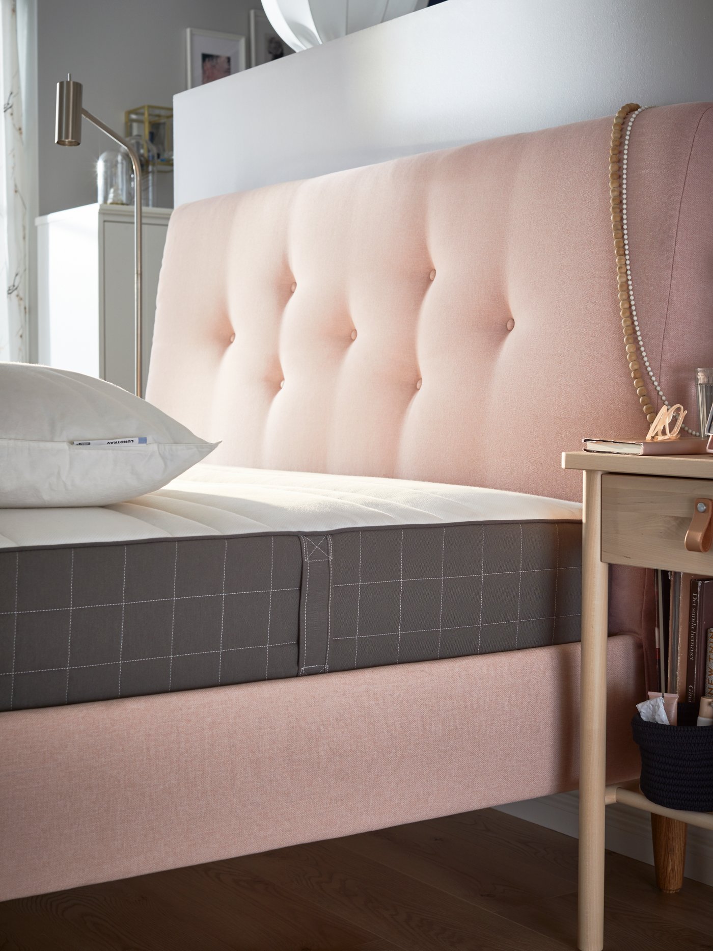 A bedroom with a blue TUFJORD upholstered bed frame, a bare white mattress and folded white duvets on top.
