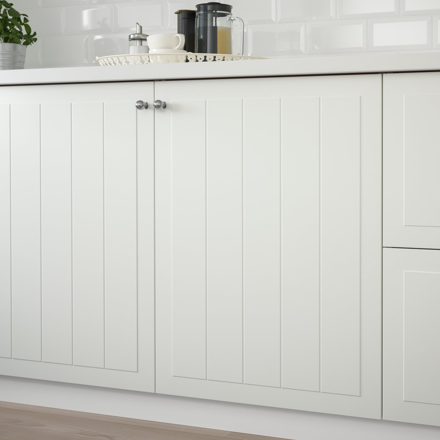Køkkenskabe med STENSUND fronter i hvid med panel låger og knopper samt en hvid bordplade, hvor der står en bakke ovenpå.
