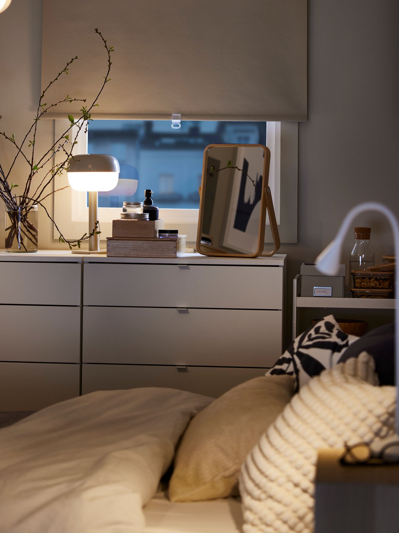 A white FÖNSTERBLAD block-out roller blind halfway down on a window that’s above two white VIHALS chests with 4 drawers.