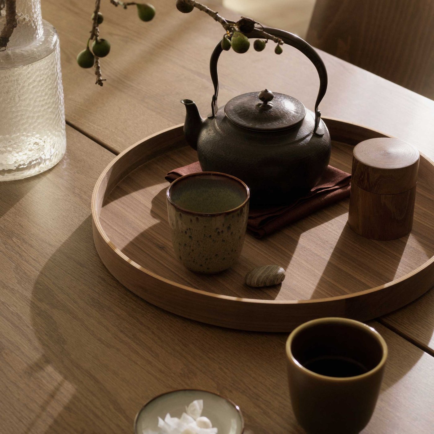 丸い木のトレイ、その中に黒い鉄の急須、陶器の湯のみ、茶筒、そして小さな石が置かれている。