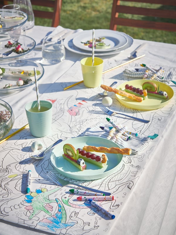 Bei einer Party im Freien sind zwei Gedecke für Kinder mit MÅLA Filzstiften und JÄTTELIK Malpapierrolle als Tischsets ausgestattet.