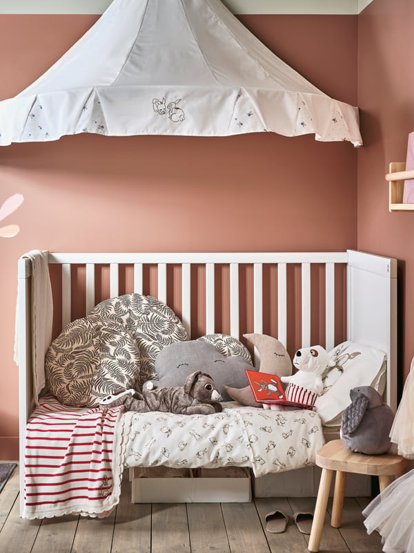 A children’s room where a SUNDVIK cot with cosy cushions and soft toys sits under a white RÖDHAKE bed canopy.