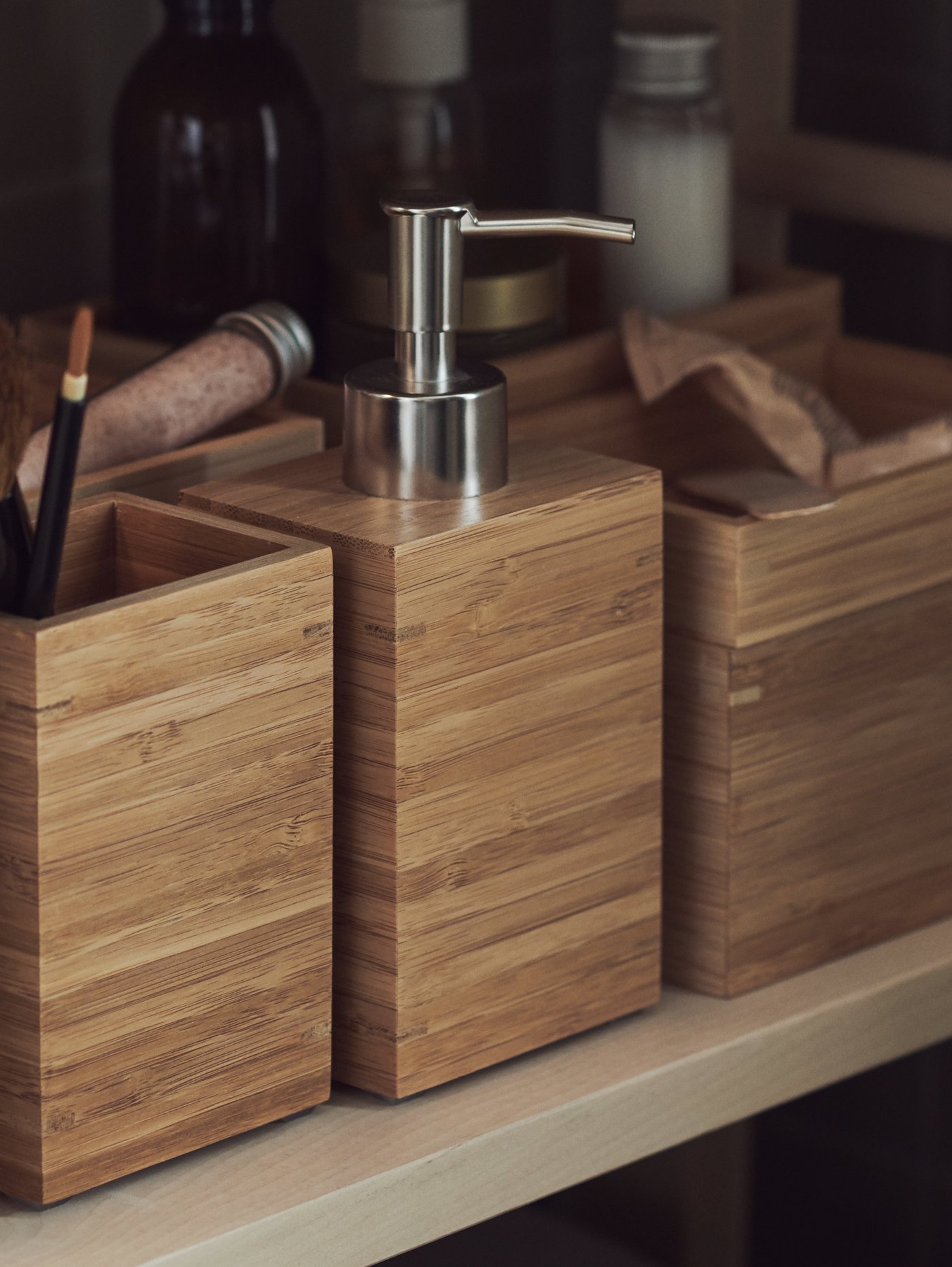 DRAGAN bathroom storage containers in materials like bamboo and cork with bottles in the background.