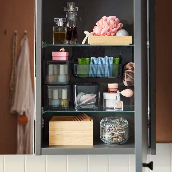 Close-up of a dark grey HAVBÄCK wall cabinet with open door, displaying organised toiletries and bathroom accessories.
