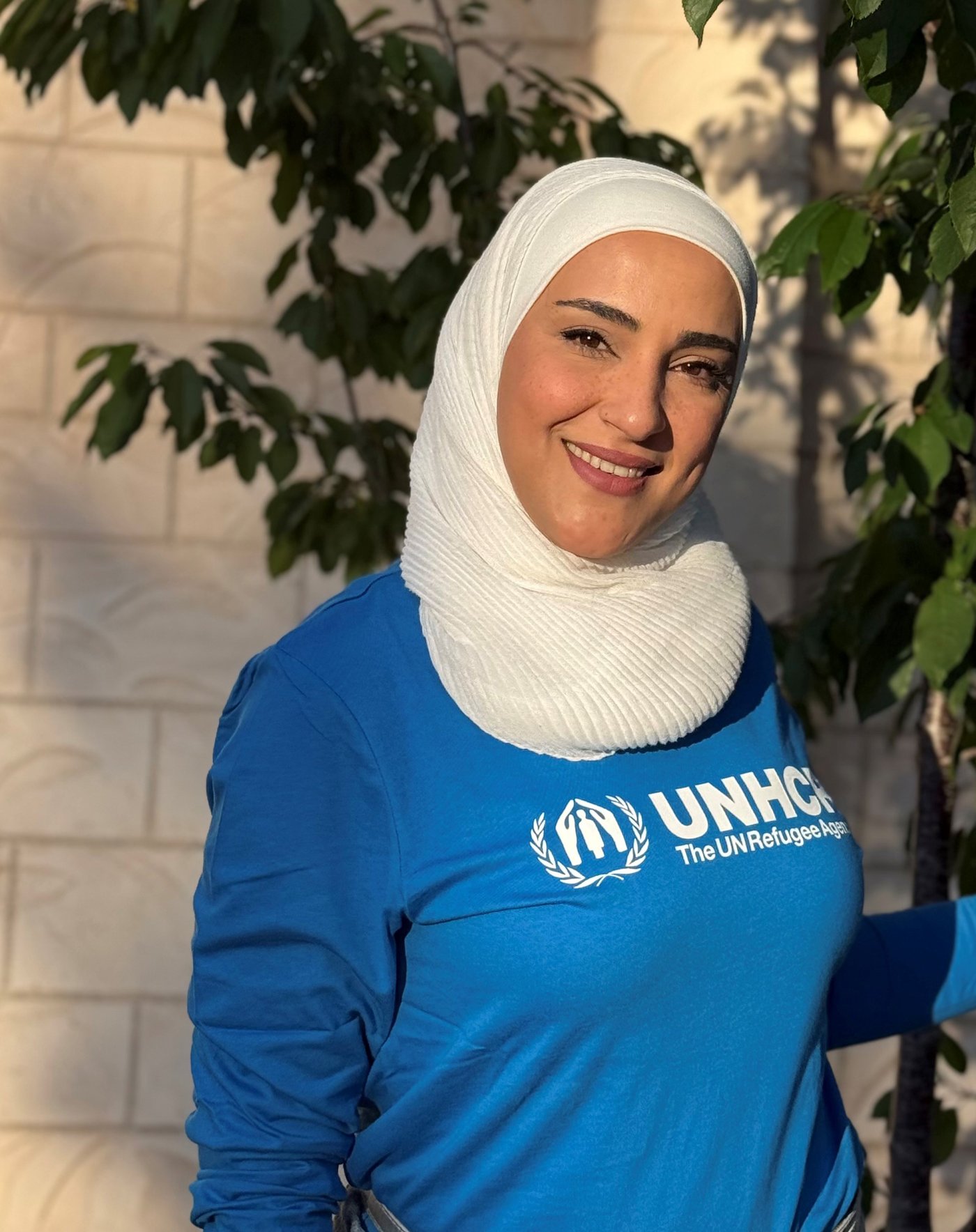Lujain steht draussen in der Abendsonne, sie trägt einen blauen UNHCR-Pullover.