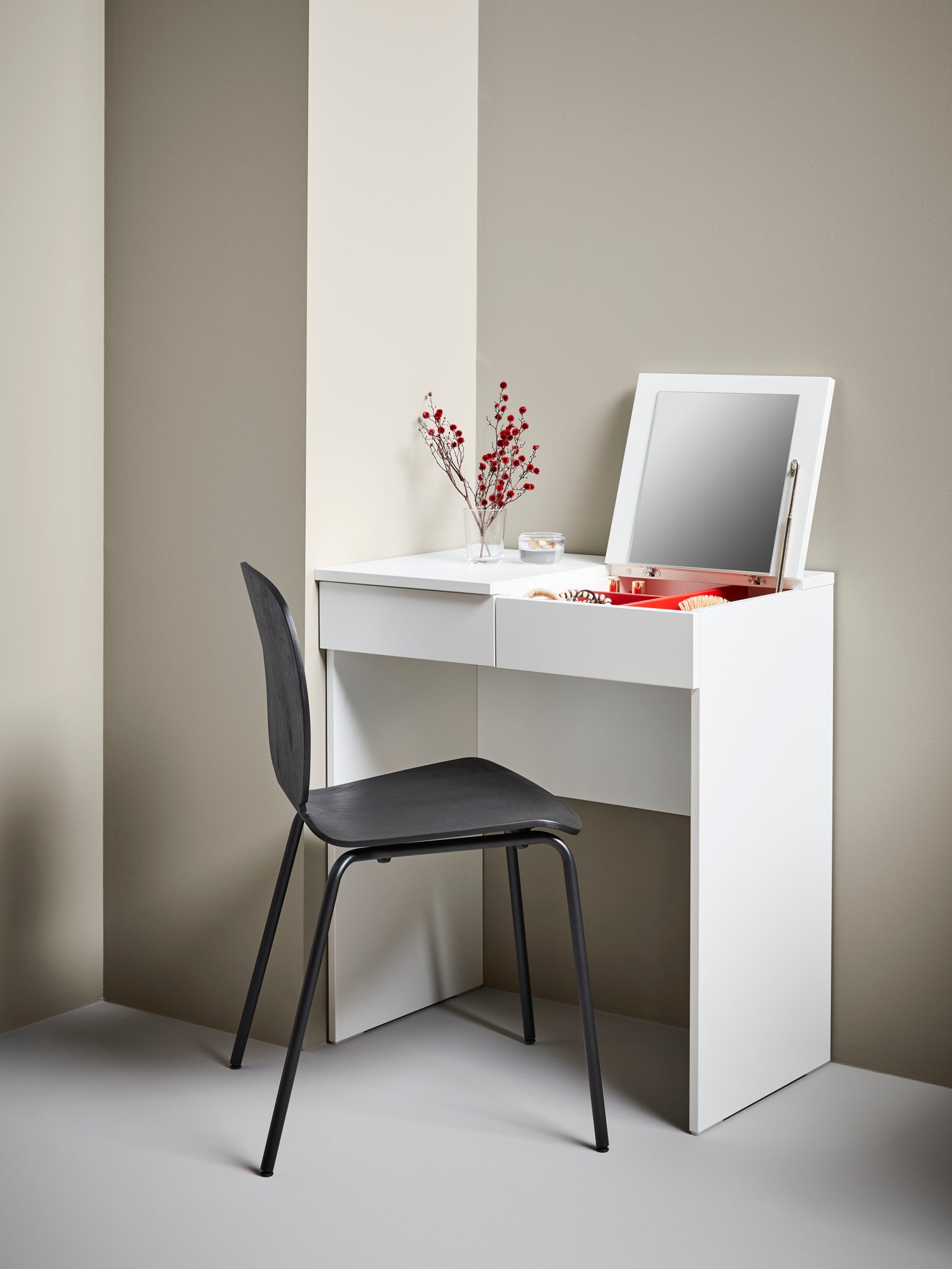 Minimalist white BRIMNES dressing table with mirror and black chair. Decorated with red flowers in a vase and a few books.