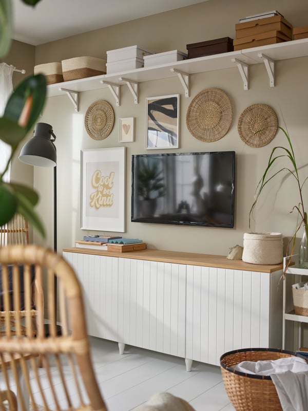 A white and light brown HEMNES TV storage bench and plenty of wall decoration around a black TV, and above it a white shelf.