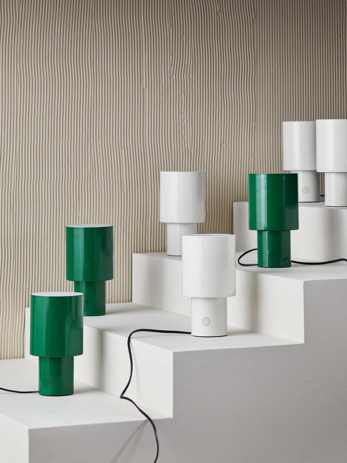 Seven SPETSBOJ table lamps in a white staircase. Half of the lamps are white, the other half are green.