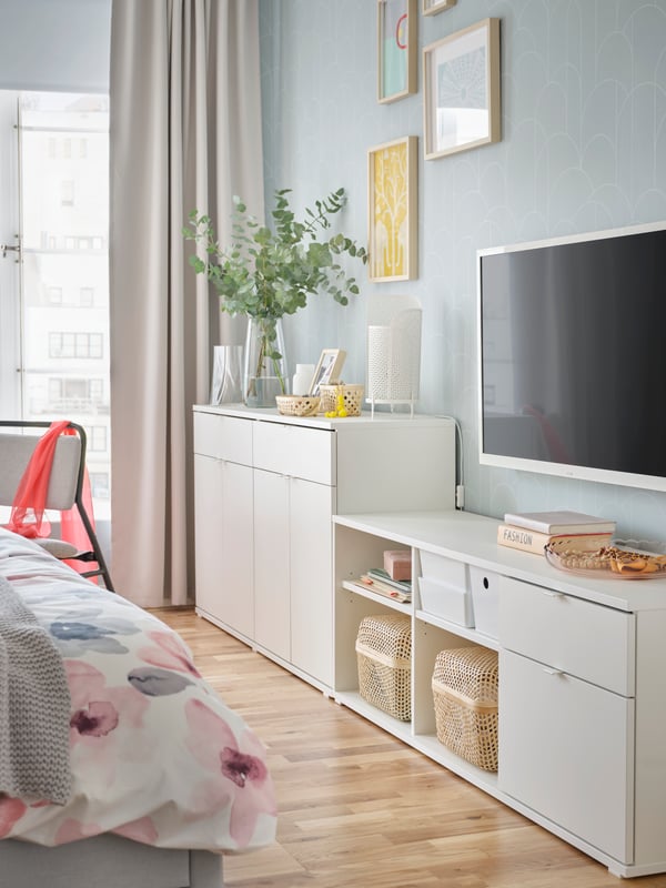 Kabinet TV VIHALS berwarna putih terletak bersandar pada dinding bilik tidur di bawah TV lekap dinding dan di sebelah saidbod VIHALS berwarna putih.