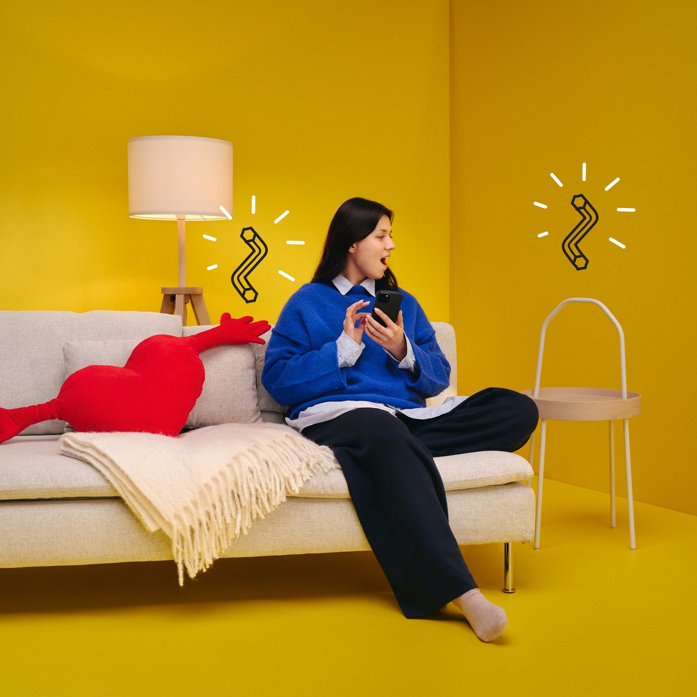 Kvinna i blå tröja som sitter i en soffa och håller en mobiltelefon, tittandes på en bild av en insexnyckel ovanpå ett soffbord