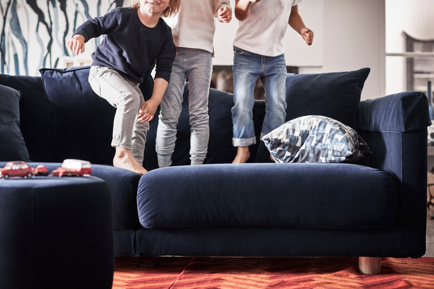 Троє дітей босоніж стрибають на синьому дивані IKEA.