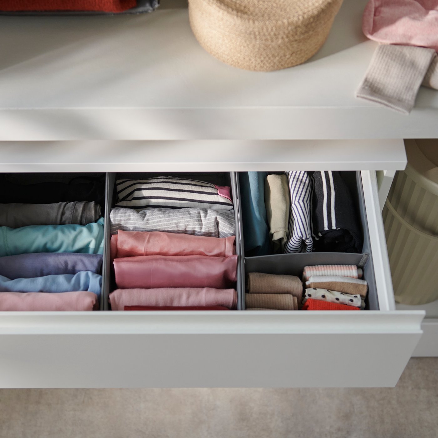 A close-up of a dark grey SKUBB box set of three, neatly organized with folded clothes in various colours inside a drawer