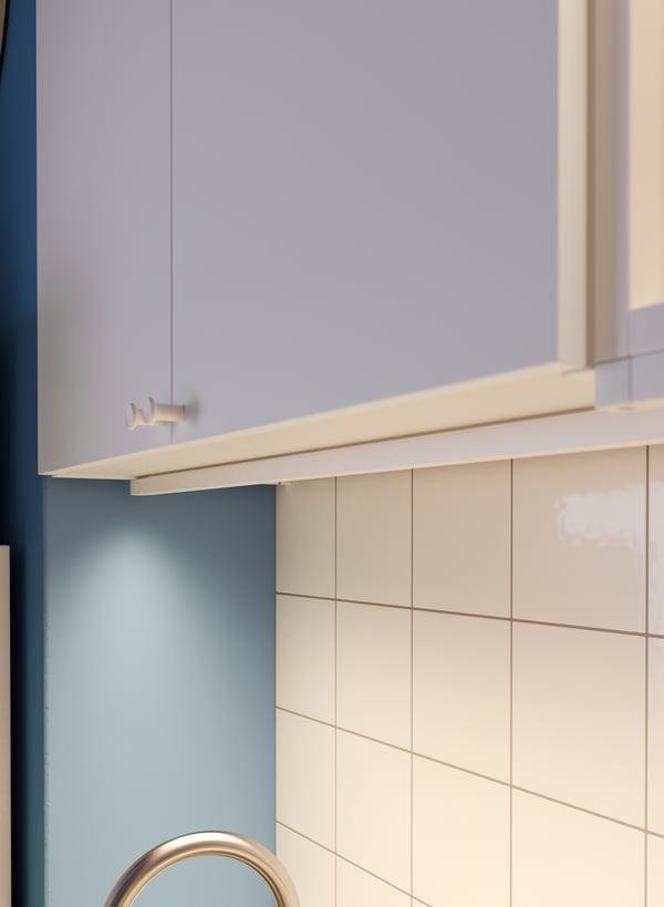 Foco largo de luz LED con sensor SKYDRAG integrado en la parte inferior de un mueble de cocina blanco empotrado a muro, sobre el lavaplatos.