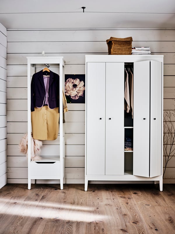 A white IDANÄS wardrobe with a basket on top beside a white IDANÄS open wardrobe, both filled with clothes.