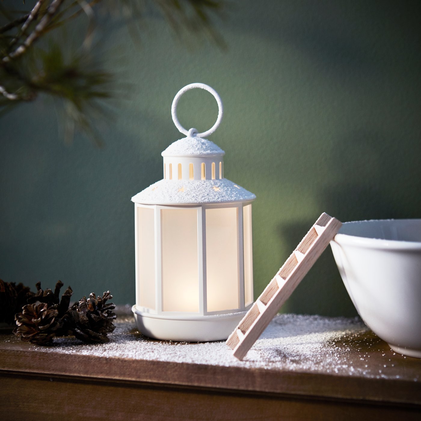 A white STRÅLA LED lantern brightens a mantelpiece frosted with artificial snow. A bowl with a mini ladder is beside it.