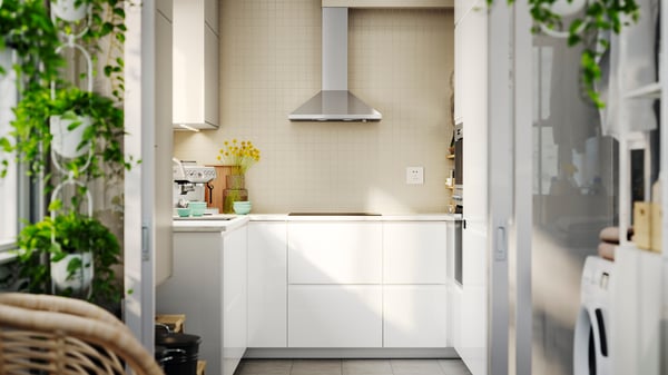 A kitchen with VOXTORP high-gloss white fronts with integrated handles, and decor touches like plants and colourful cups.