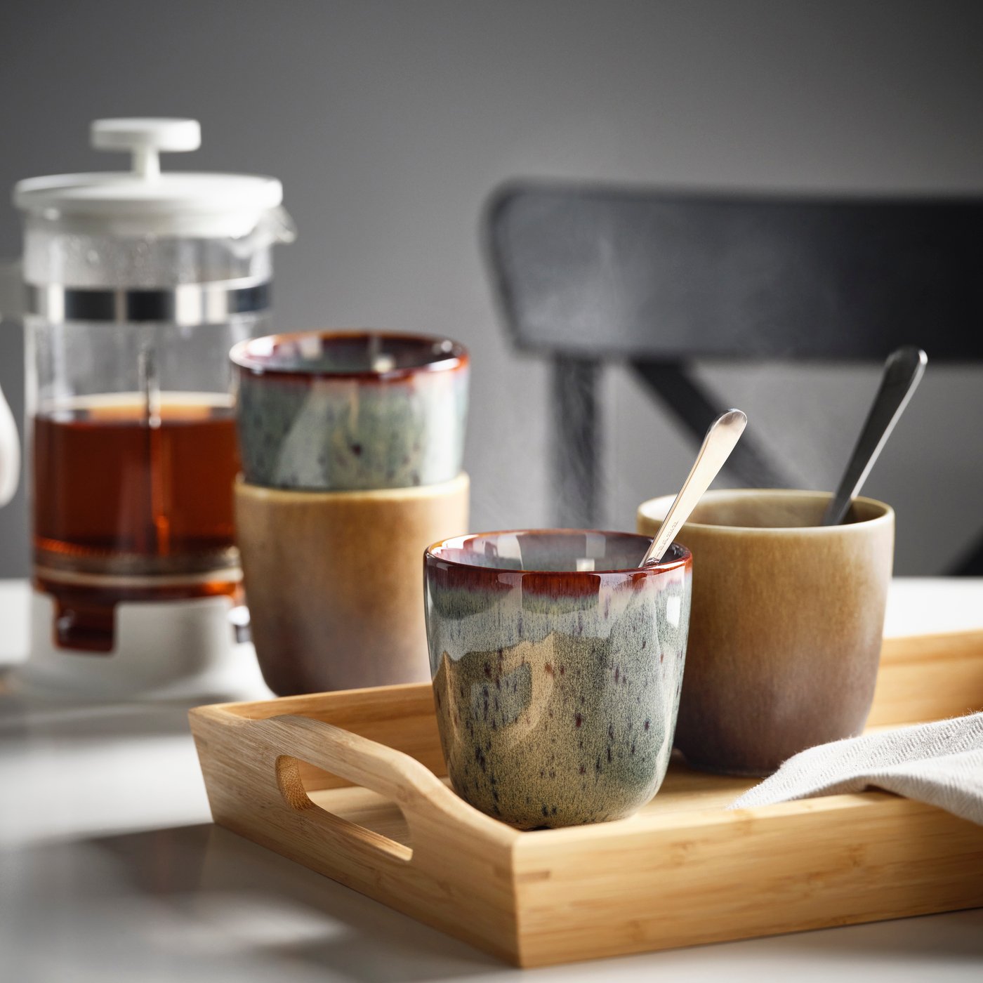Trendige Kaffeetassen aus Keramik und eine Kaffeepresse stehen auf einem Tisch.