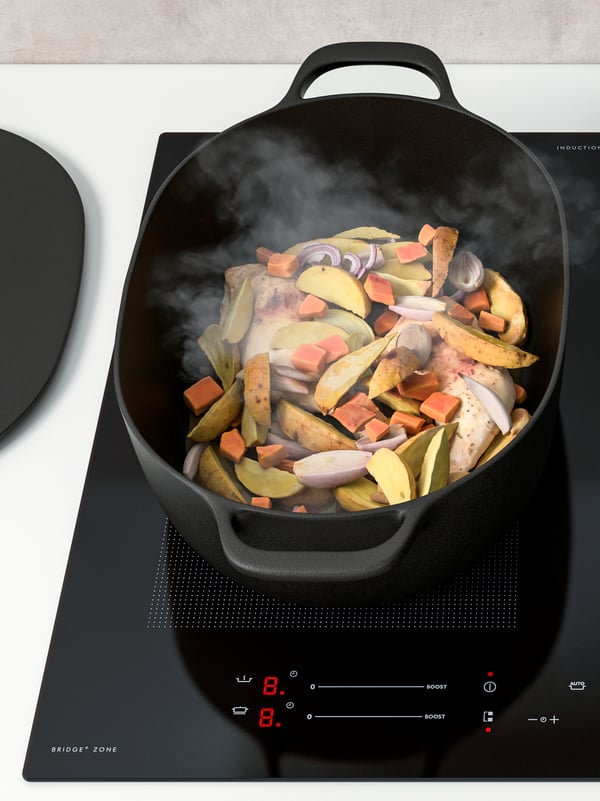 An induction hob with a black VARDAGEN cast-iron pot cooking a one-pot meal of veggies, potatoes and chicken.
