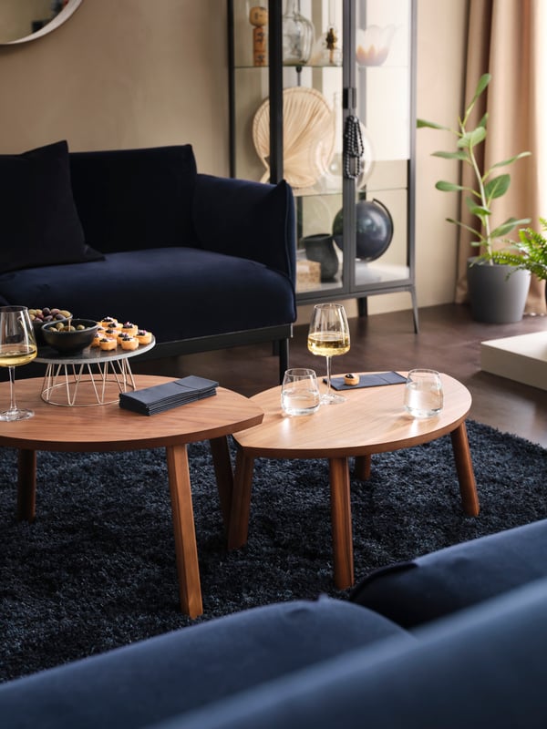 Dua sofa ÄPPLARYD menghadap antara satu sama lain dengan dua meja STOCKHOLM yang mempunyai makanan dan gelas berisi wain dan air terletak di antara kedua-dua sofa itu.