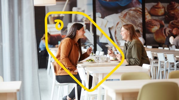 Two people seated at a café table having a conversation, with one person highlighted by a yellow outline.