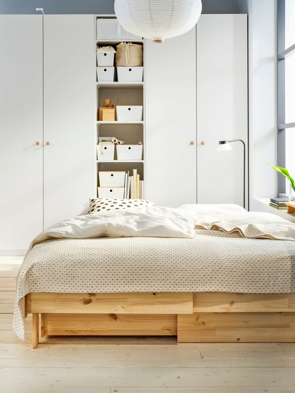 In una camera da letto, un guardaroba bianco e un letto allungabile con contenitore GLAMBERGET in pino con un copriletto chiaro.