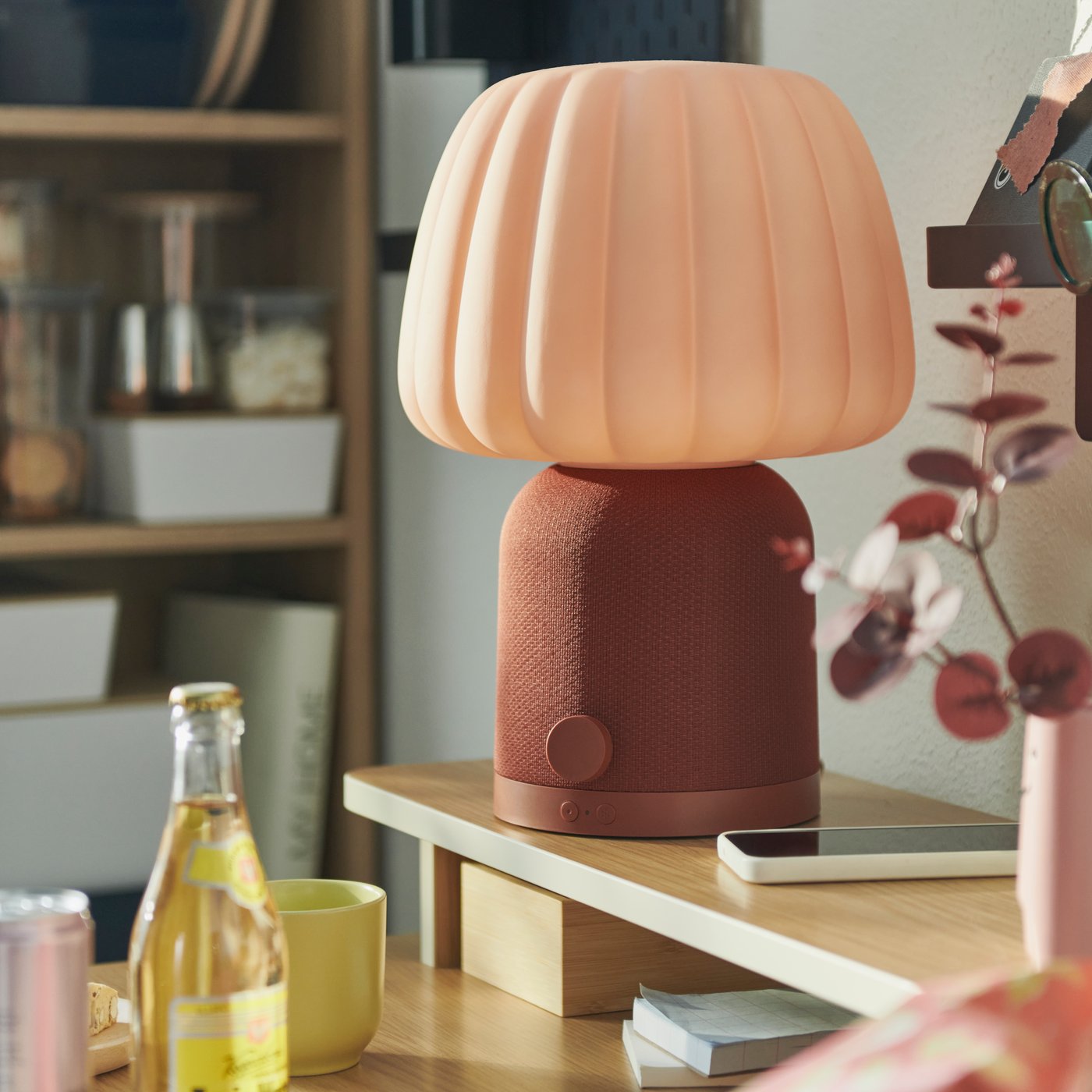U studentskoj sobi nalazi se KULGLASS Bluetooth zvučnik-lampa smeđe-roze boje na drvenom stolu, sa sokom u prvom planu.