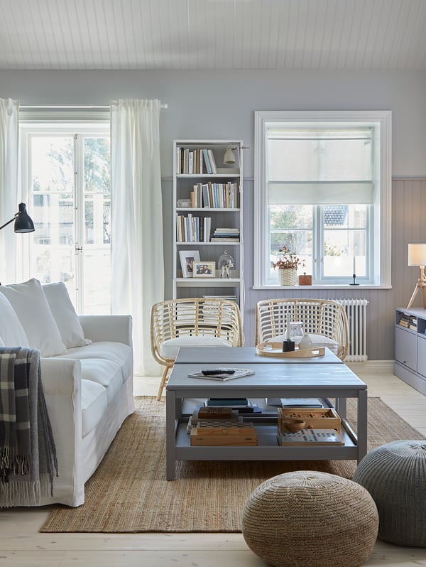 Two HAVSTA coffee tables sit on a rug with a GRÖNLID sofa, two pouffes and two rattan armchairs at the edges of the rug.