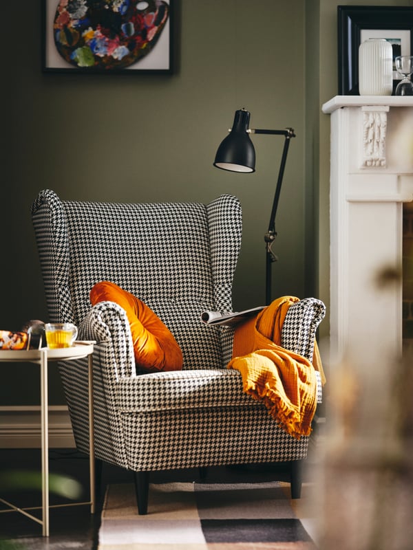A black/beige STRANDMON wing chair between an anthracite ARÖD floor/reading lamp and a dark grey-beige GLADOM tray table.