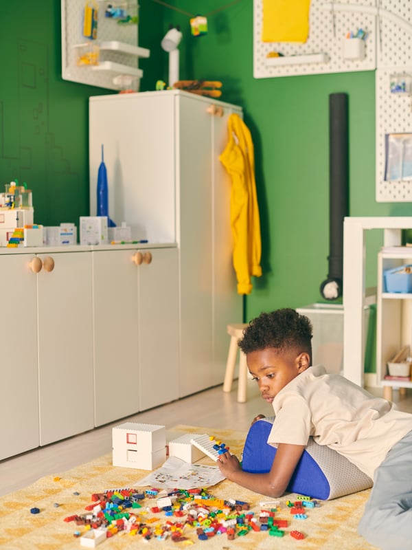 A boy lies next to a BYGGLEK LEGO mixed-colour brick set scattered on the floor of a green room.