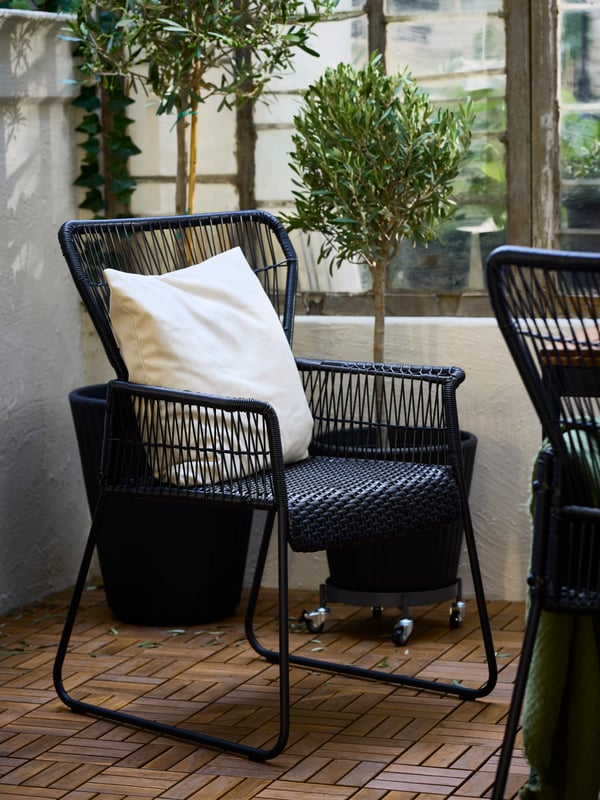 En hynde med et HJÄRTERÖ hyndebetræk i en antracit TALLSKÄR stol med armlæn på en terrasse med RUNNEN terrassebelægning.