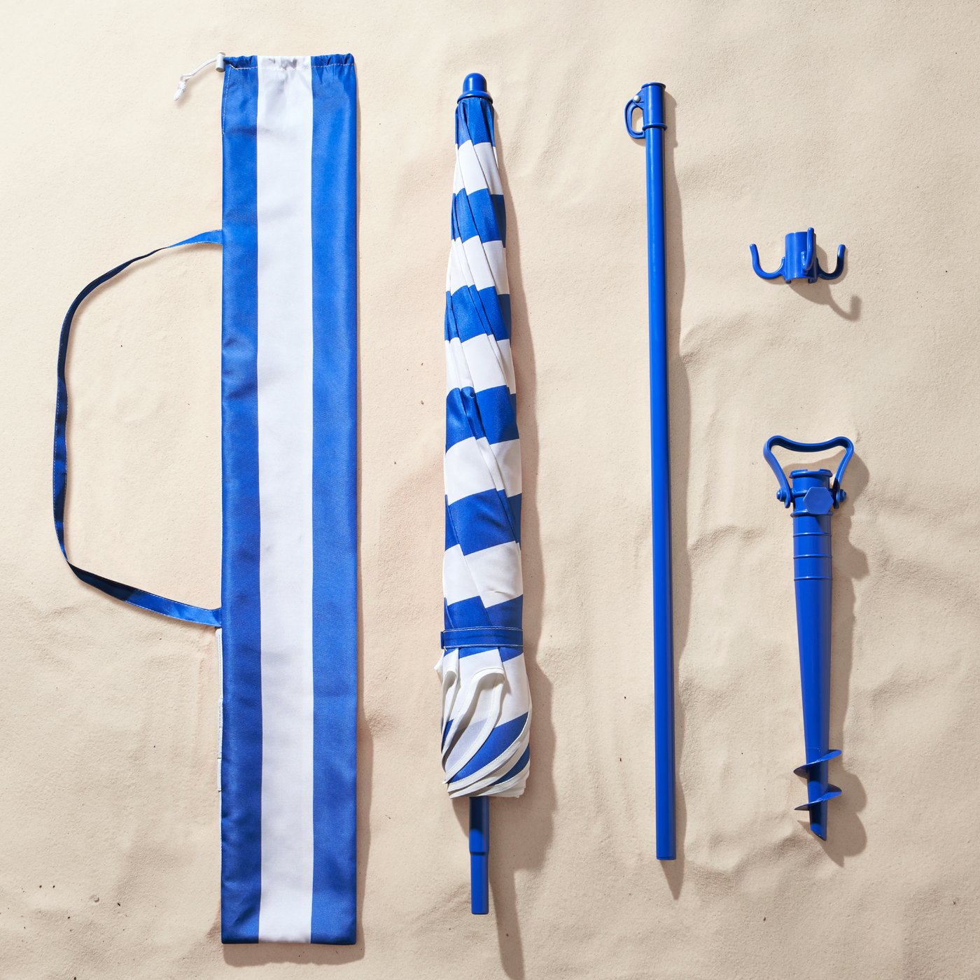 Vus d’en haut, éléments du parasol STRANDÖN et son sac de transport disposés sur le sable.