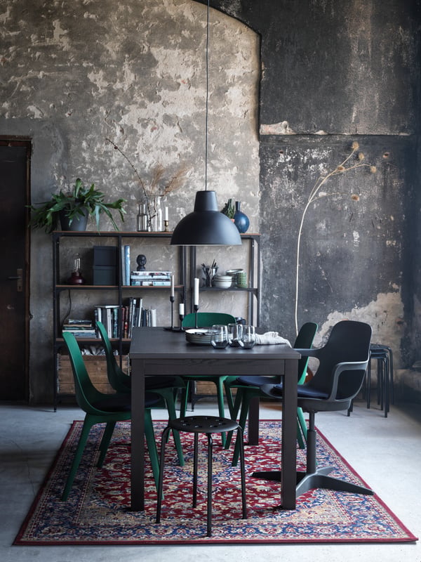 A dining area formed by a brown LANEBERG table and various chairs and stools, all standing on a multicolour VEDBÄK rug.