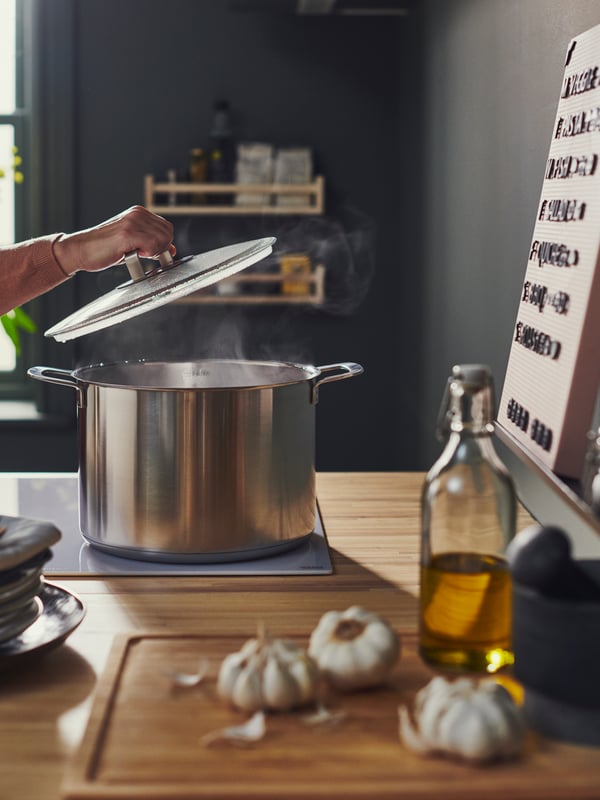 대나무 APTITLIG 압티틀리그 도마 옆의 화구에 놓인 스테인리스스틸 IKEA 365+ 이케아 365+ 압력솥의 뚜껑을 열고 있는 사람.